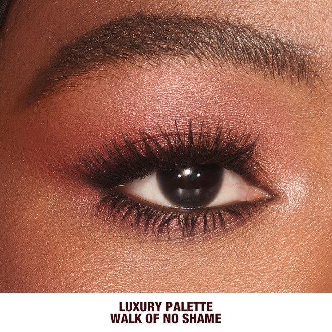 Single-eye close-up of a brown-eyed deep-tone model wearing shimmery berry-pink eye makeup.