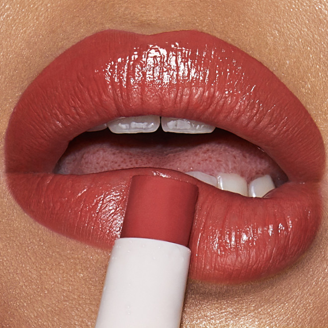 Lips close-up of a medium-tone model applying a moisturising lipstick lip balm in a peachy nude rose shade.