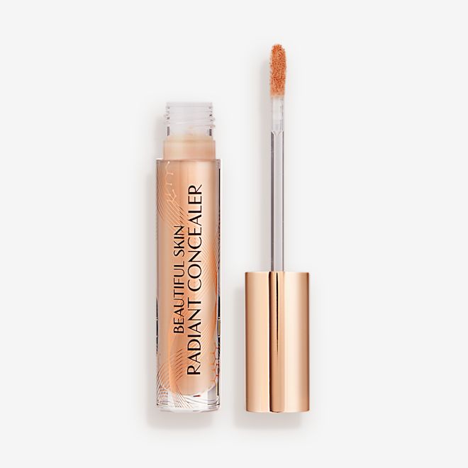 Beautiful Skin Radiant in Concealer in 9 lid removed Radiant concealer in a glass tube with its doe-foot applicator next to it with a gold-coloured handle.