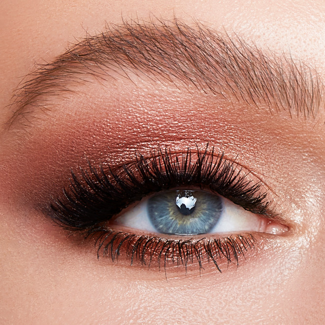 Single-eye close-up of a fair-tone model with blue eyes with shimmery rose gold and brown eye makeup. 