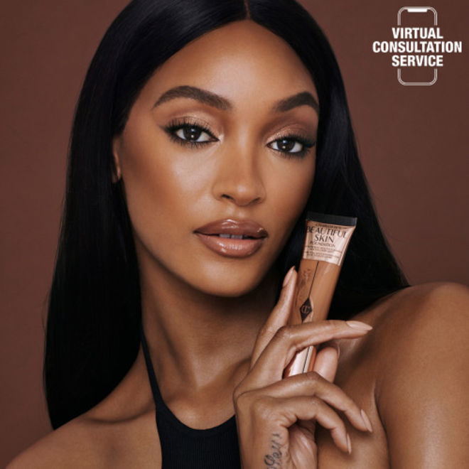 Charlotte's Beautiful Skin Foundation on deep-tone model Deep-tone model wearing shimmery brown eye makeup with nude pink lip gloss, and luminous, skin-like foundation.