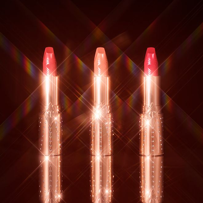 Kissing Lipsticks trio open Three open lipsticks in the shades peachy-nude, rose pink, and bright pink in gold-coloured tubes with sparkles all over.