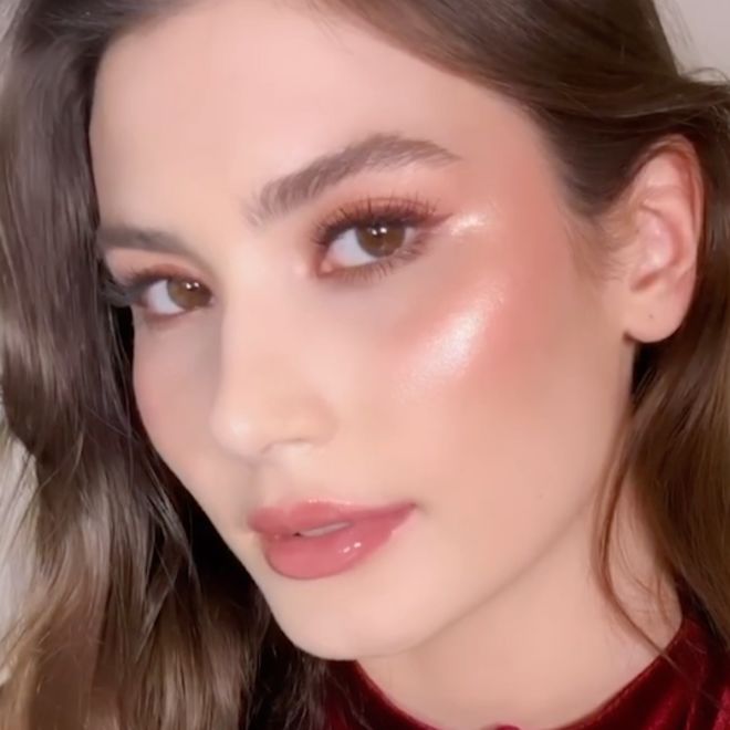 Beauty Light Wand in Pillow Talk Original on light skin A light skin, brunette model wearing natural glam makeup and an illuminating, pinkish-golden highlighter.