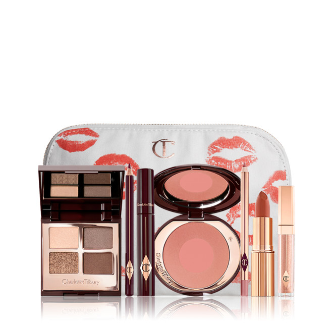 An open, mirrored-lid eyeshadow palette in matte and shimmery gold, brown, and beige shades, an open black eyeliner pencil, a mascara in a dark-crimson colour scheme, a golden-peach lipstick with a nude pink lip liner pencil, nude-peach lip gloss, and an open two-tone blush in muted brown-pink. 