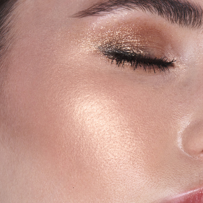 Close-up of a fair-tone model wearing shimmery gold eyeshadow with a glowy yet subtle, pearlescent highlighter in a rose-gold shade.