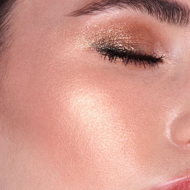 Hollywood Superstar Glow Highlighter on fair-tone model close-up Close-up of a fair-tone model wearing shimmery gold eyeshadow with a glowy yet subtle, pearlescent highlighter in a rose-gold shade.
