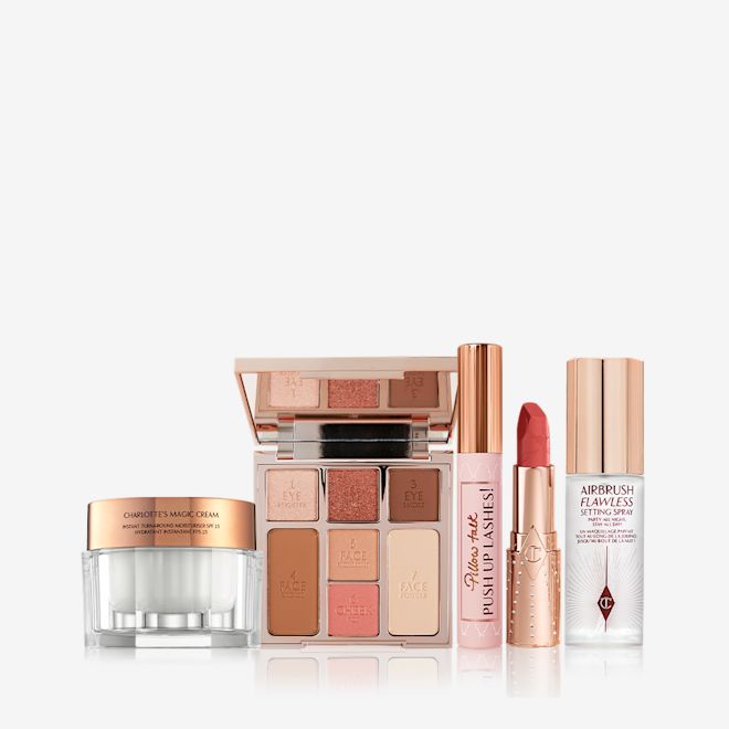 Look of Love bundle 3 displayed An open, mirrored-lid face palette with nude eyeshadows, nude pink and soft pink blushes, bronzer, and highlighter, an open lip liner pencil in nude pink shade, black mascara with nude pink tube with a gold-coloured lid, an open lipstick in a coral-pink shade in a gold-coloured tube, pearly-white cream in a glass jar with a gold-coloured lid, and setting spray with a gold-coloured lid.