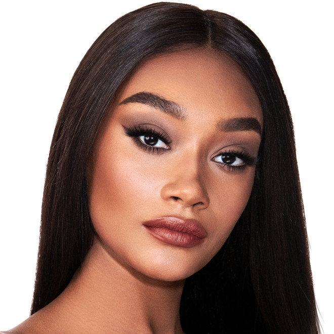 A deep-tone model with brown eyes wearing smokey brown eye makeup with muted pink blush and glossy terracotta-brown lips