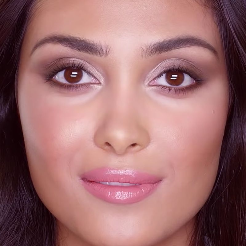 A light-tone brunette model with brown eyes wearing a smokey mauve eye look with glowy rosy cheeks, and glossy bright pink lips. 