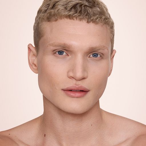 Airbrush Flawless Concealer - 5.5 medium model after Close-up of a hand holding a rose-gold tube of Charlotte Tilbury Airbrush Flawless Foundation, with the product name partially visible. The background features smooth, dark hair cascading down, creating a sleek and elegant contrast.