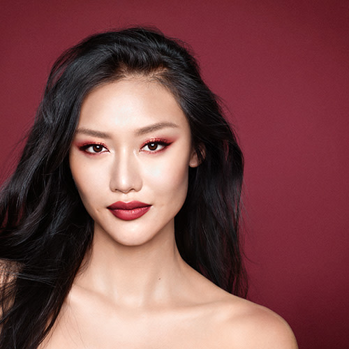 Model wearing a red sparkly eye makeup look with bold red lipstick
