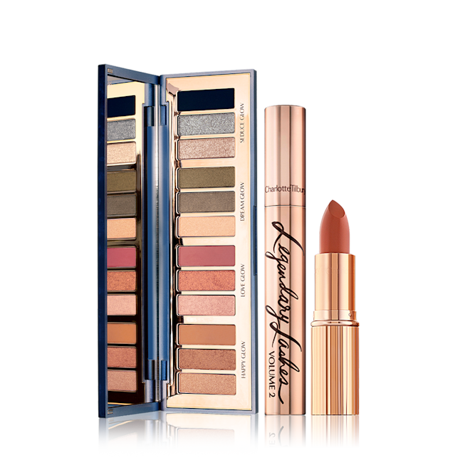 Starry Eye and Lip Kit open An open, mirrored-lid eyeshadow palette with eyeshadows in shades of pink, brown, peach, golden, blue, and green, along with a mascara with gold packaging, and an open lipstick in a medium-dark coral shade.