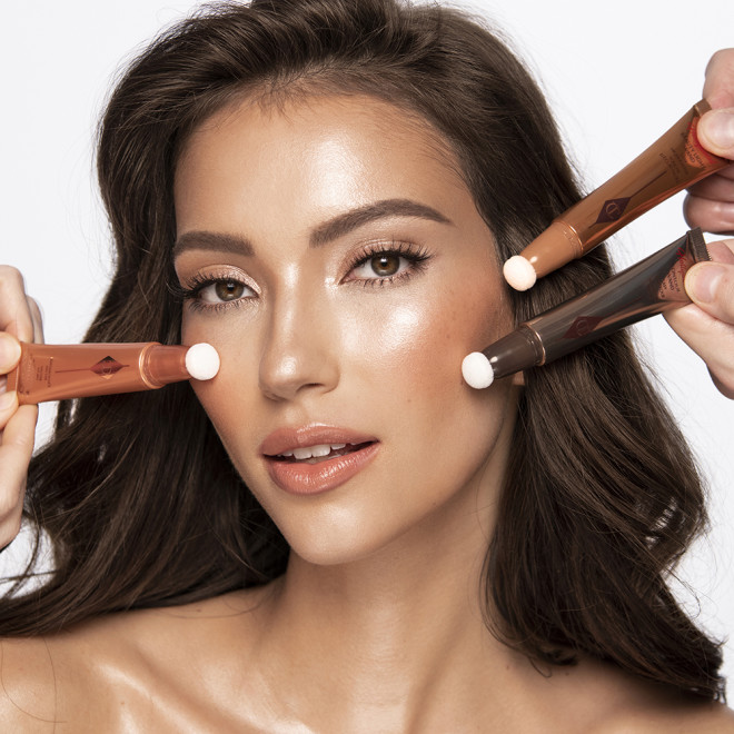Medium-tone brunette model wearing glowy, nude coral-pink soft glam makeup look while getting blush and contour applied from liquid highlighter blush wands and a liquid contour wand.