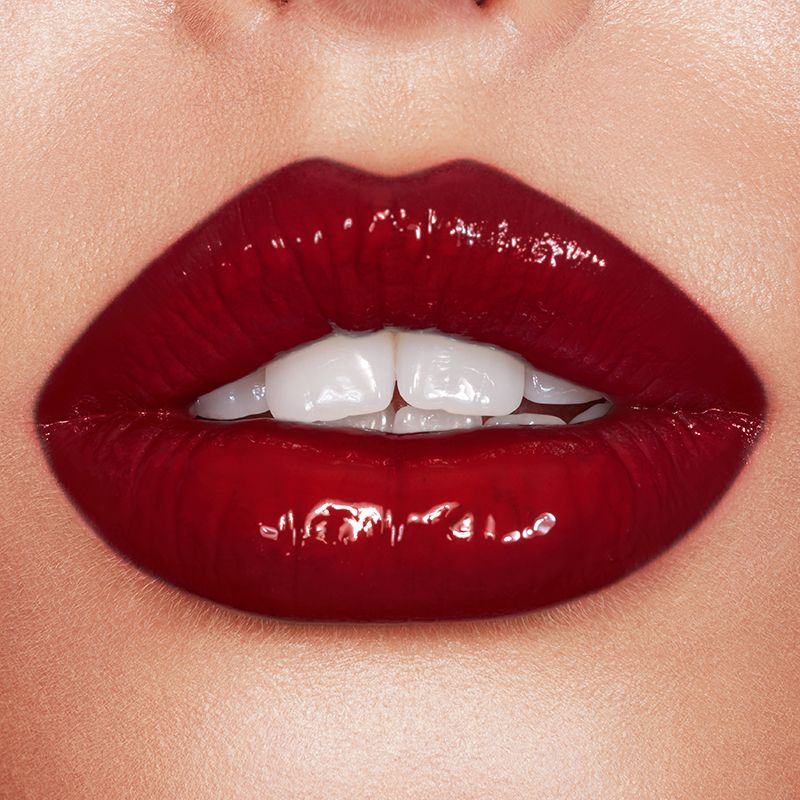 Lips close-up of a fair-tone model wearing a vivid, opaque, crimson-red lip gloss. 