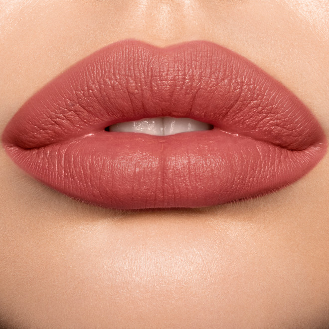 Lips close-up of a light skin model wearing a pigmented, matte lipstick in a golden peachy-pink colour. 