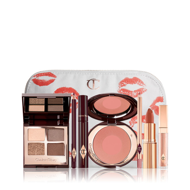 An open, mirrored-lid eyeshadow palette in matte and shimmery gold, brown, and beige shades, an open black eyeliner pencil, a mascara in a dark-crimson colour scheme, a golden-peach lipstick with a matching lip liner pencil, nude-peach lip gloss, and an open two-tone blush in muted brown-pink. 
