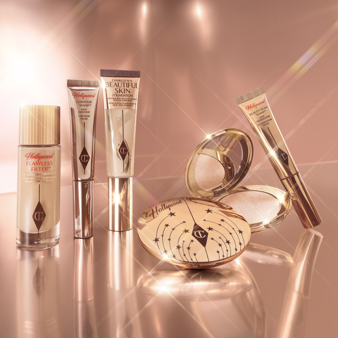 Tinted primer in a glass bottle with a gold-coloured lid, contour, foundation, and highlighter wands, and setting powder and powder highlighter compacts in sleek gold packaging.