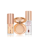 Travel-size kit that includes a glowy primer in a glass bottle with gold-coloured lid, face powder compact in a light shade with a mirrored-lid in gold-coloured packaging, and setting spray in a clear bottle with gold-coloured lid.