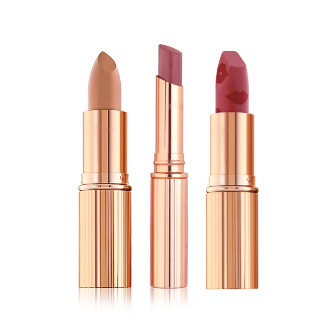 Three open lipsticks, one a satin finish nude sandy brown, glossy lipstick in a berry-pink shade, and matte lipstick in a nude berry-pink shade, with all three in gold-coloured tubes.