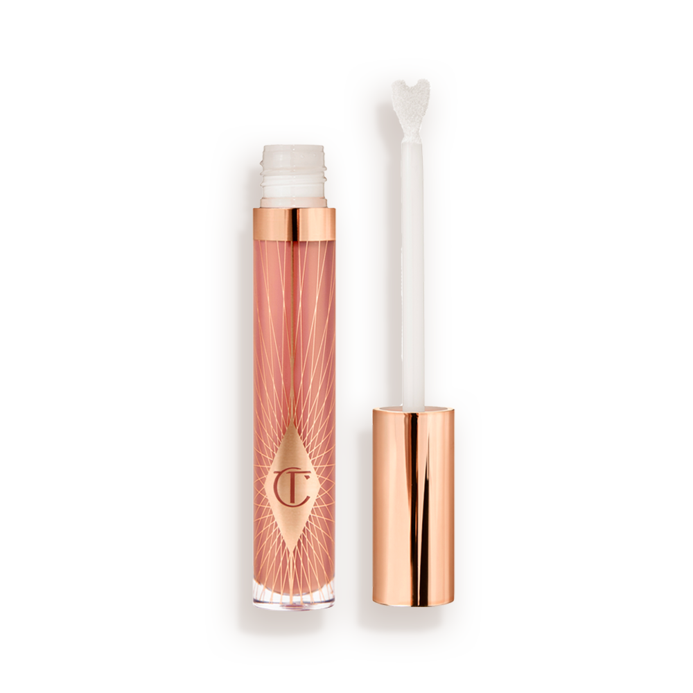 Collagen Lip Bath Lip Gloss en Pillow Talk con la tapa quitada Un brillo de labios abierto, de tamaño estándar, de color nude rosa, con un aplicador en forma de corazón y una tapa de color oro rosa al lado.