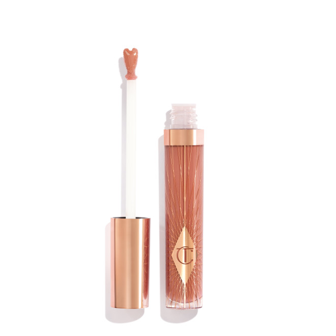 an opened, standard-sized, nude-pink lip gloss with a heart-shaped applicator with a rose gold lid next to it. 