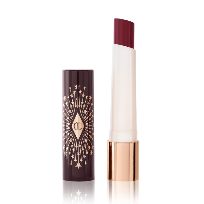 An open lipstick lip balm in a berry shade, in white and gold tube with a black-coloured lid with gold sparkles all over it.