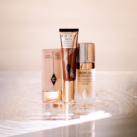 Foundation in a clear plastic bottle with a sleek gold coloured lid, foundation wand with gold packaging and a dark brown body that's the colour of the foundation inside along with a gold-coloured lid, and foundation in a frosted glass bottle with a gold-coloured lid.