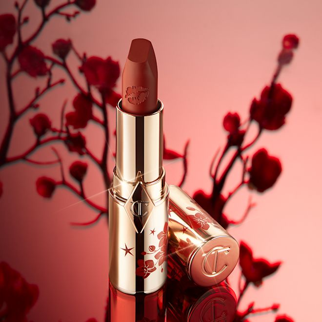 Matte Revolution lipstick in Blossom Red open A matte burnt-orange red lipstick in gold-coloured packaging with cherry blossoms illustrated on the tube for the Lunar New Year, along with its lid next to it.
