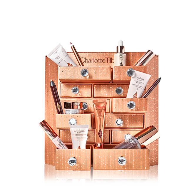 Charlotte's Bejewelled Chest of Beauty Treasures open A golden-coloured chest of drawers with a clay mask, nude pink matte lipstick, nude pink lip liner, eyeliner pencil in dark copper, black-coloured mascara, liquid primer, champagne-coloured liquid highlighter, dark brown eyeliner pencil, pearly-white face cream, luminous ivory-coloured serum, and bronze-coloured body highlighter.