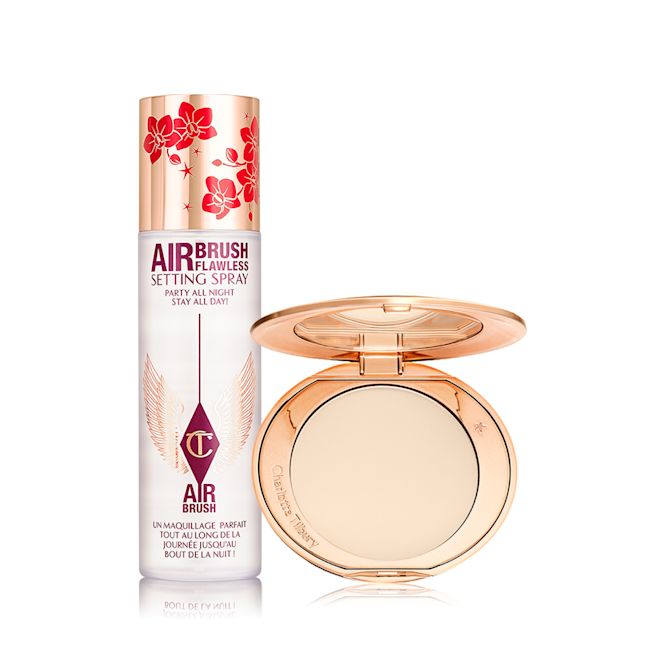 Airbrush Flawless Lucky New Year Kit A makeup setting face mist in a large, clear bottle with gold and red blossom details on the lid in celebration of the lunar new year and an open, pressed powder compact for fair skin tones with a mirrored lid, in gold-coloured packaging with red-coloured cherry blossoms on the lid.