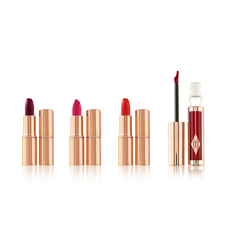 Three open lipsticks with an open lip gloss in bright shades of pink, red, and purple with their lids next to them. 