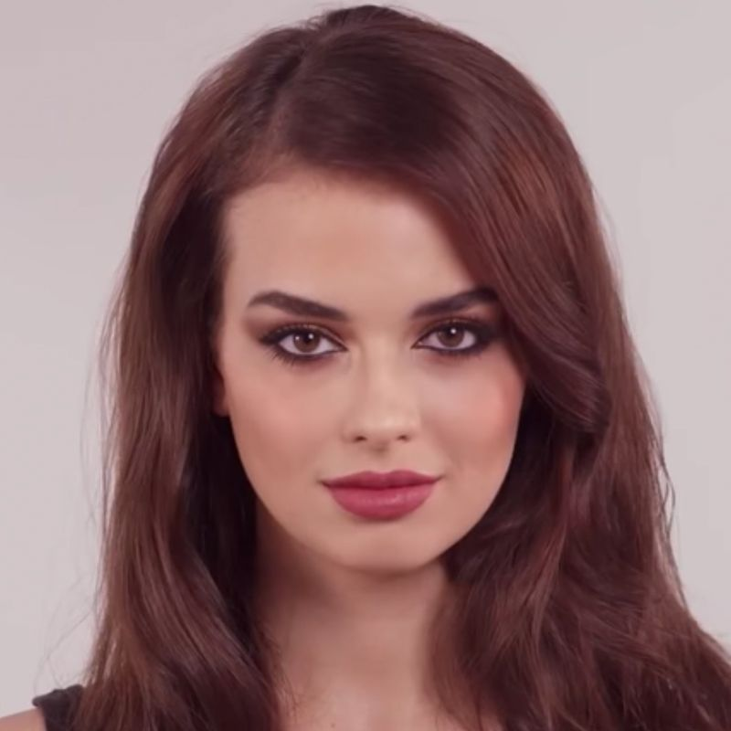 A light-tone model with brown eyes with shimmery copper, gold, and brown eye makeup with black eyeliner and matte, berry-pink lips. 