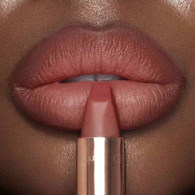 Lips close-up of a deep-tone model wearing a matte lipstick in a delicate peachy nude colour. 