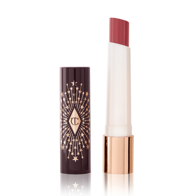An open lipstick lip balm in a sheer peach rose shade, in white and gold tube with a black-coloured lid with gold sparkles all over it.