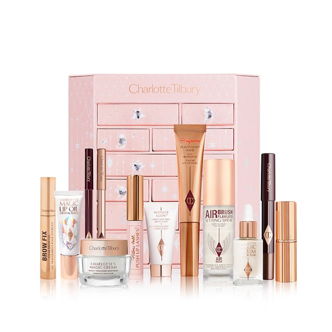 Charlotte Tilbury Advent Calander 2022 Chest with products displayed A pink-coloured chest of drawers with a clay mask, nude pink matte lipstick, nude pink lip liner, eyeliner pencil in dark copper, black-coloured mascara, liquid primer, champagne-coloured liquid highlighter, dark brown eyeliner pencil, pearly-white face cream, luminous ivory-coloured serum, and bronze-coloured body highlighter.