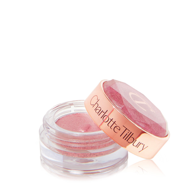 A shimmery eyeshadow pigment in a rose gold shade in a glass pot with its lid next to it.