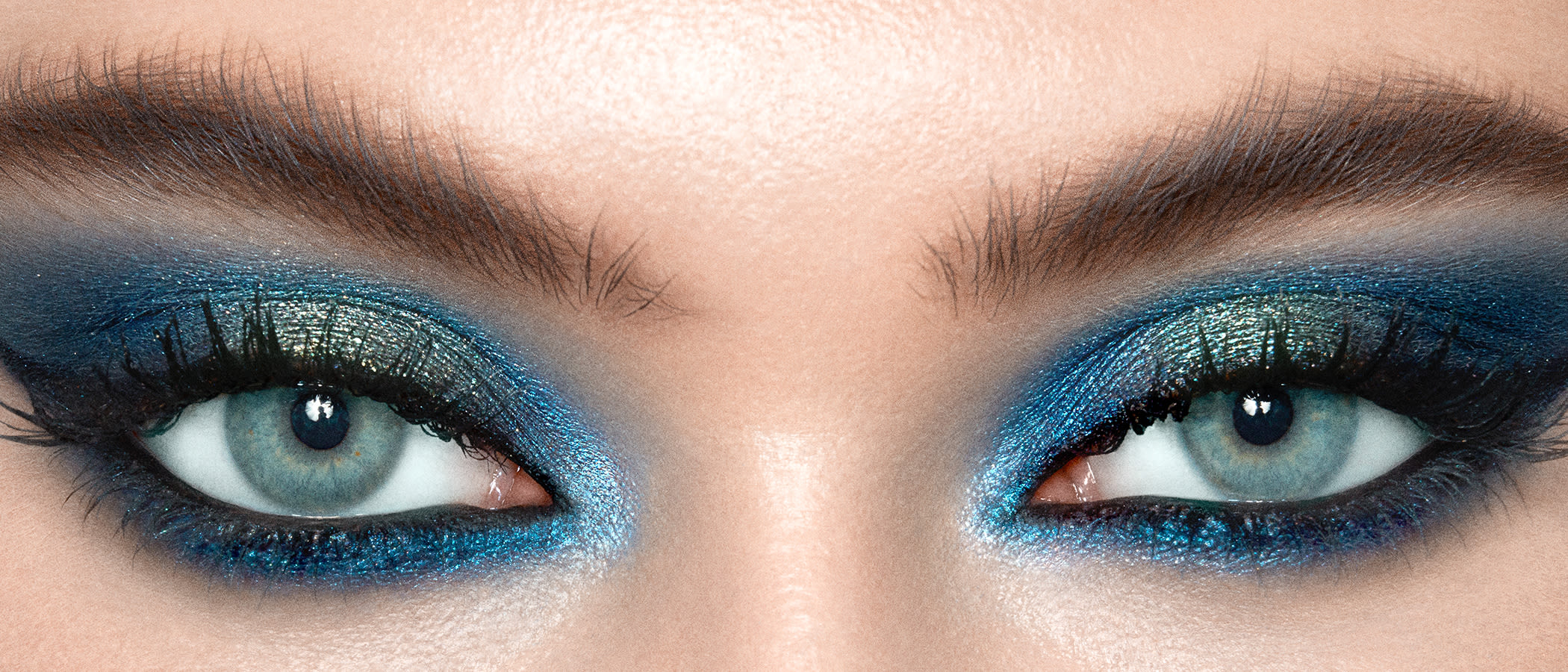 The Icons Eyeshadow Palette blue look on blue eyes close-up Close-up of a light-tone model's blue eye with shimmery, teal, royal blue, and ice blue eye makeup.