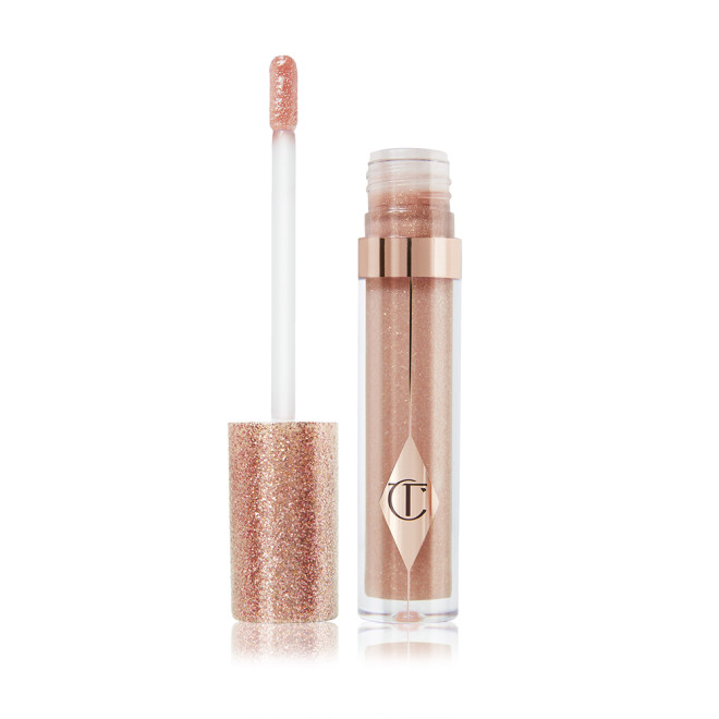 An open, shimmery lip gloss in a rosy champagne shade with fine glitter with its doe-foot applicator next to it. 