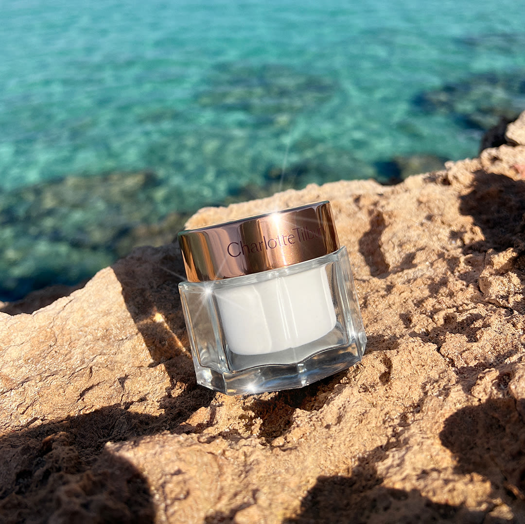 011 210588 BEAUTIFUL SKIN BRONZER SP MAGIC CREAM LM 2204 Setting spray in a clear bottle with a gold-coloured lid, highlighter wand in a golden-coloured tube with a gold-coloured lid, bronzer compact with a mirrored-lid, face cream in a glass jar, setting powder compact, and an SPF-infused primer in a white tube.