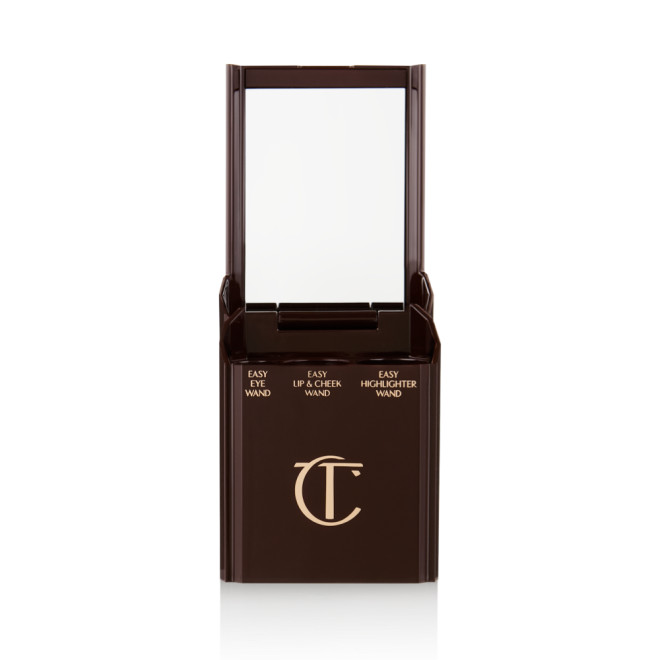 An open, black-brown-coloured portable makeup case with a mirrored lid, with three product places, which are for eyeshadow stick, lip and cheek stick, and highlighter stick.