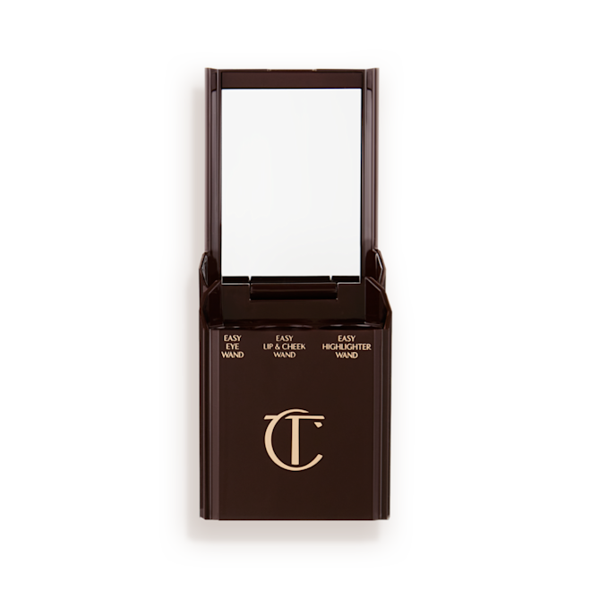 Quick & Easy Instant 5 Minute case open An open, black-brown-coloured portable makeup case with a mirrored lid, with three product places, which are for eyeshadow stick, lip and cheek stick, and highlighter stick.