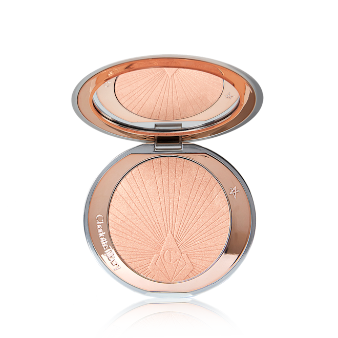 Charlotte's Hollywood Superstar Glow Powder open An open, pressed powder highlighter compact in a light pinky beige shade with a mirrored lid.