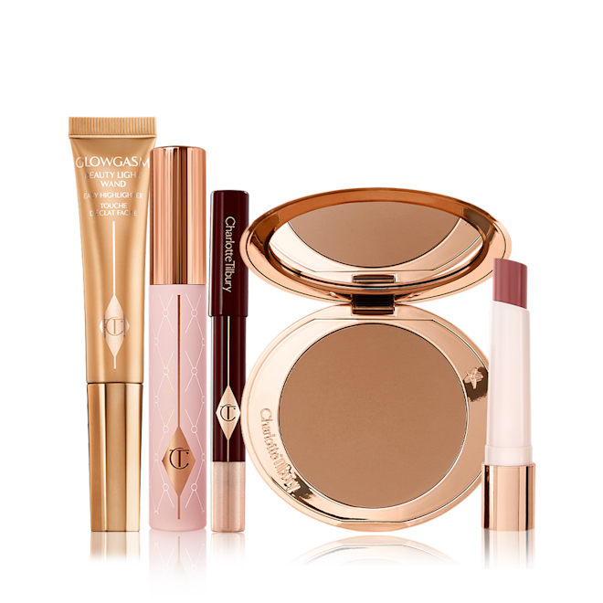 Charlotte's Power Glow Kit displayed Liquid highlighter wand in a honey gold shade, mascara in a nude pink tube with a gold-coloured lid, chubby eyeshadow stick in a champagne shade, bronzer compact with a mirrored-lid in a dark brown shade, and lipstick balm in a nude berry red shade.
