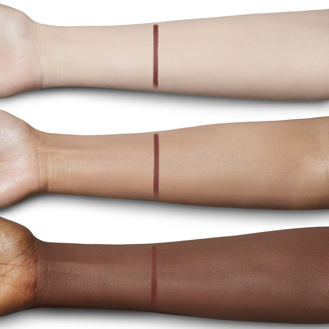 Swatch of an eyeliner in a berry-pink shade on fair, tan, and deep-tone arms.