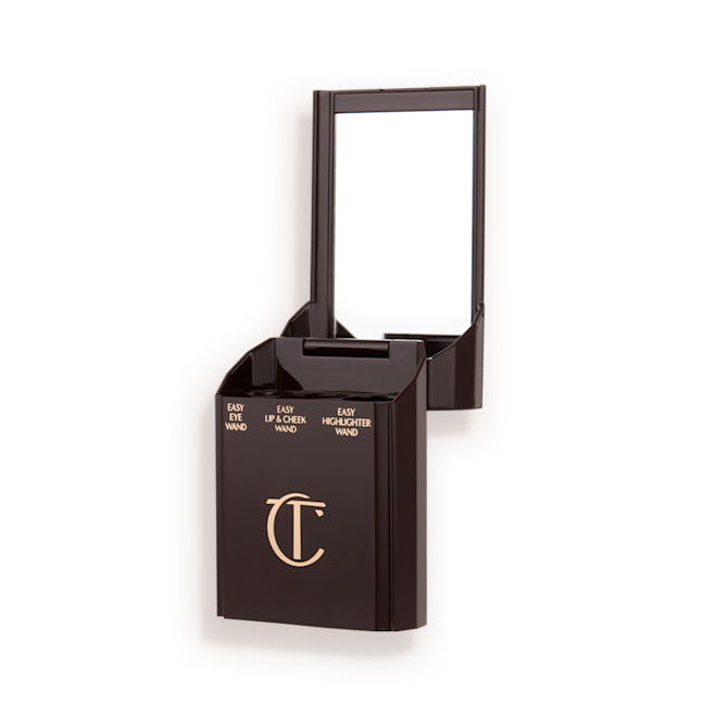 Quick & Easy Instant 5 Minute case open An open, black-brown-coloured portable makeup case with a mirrored lid, with three product places, which are for eyeshadow stick, lip and cheek stick, and highlighter stick.