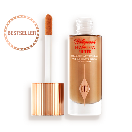 HFF-6.5-LEGENDARY-PDP 1 An open, luminous primer in a dark golden-beige shade in a glass bottle with its gold and white doe-foot applicator next to it.