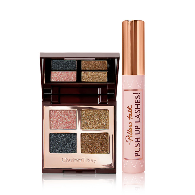 An open, mirrored-lid quad eyeshadow palette in shimmery pink, blue, and gold shades with a mascara with a nude pink tube and gold-coloured lid. 