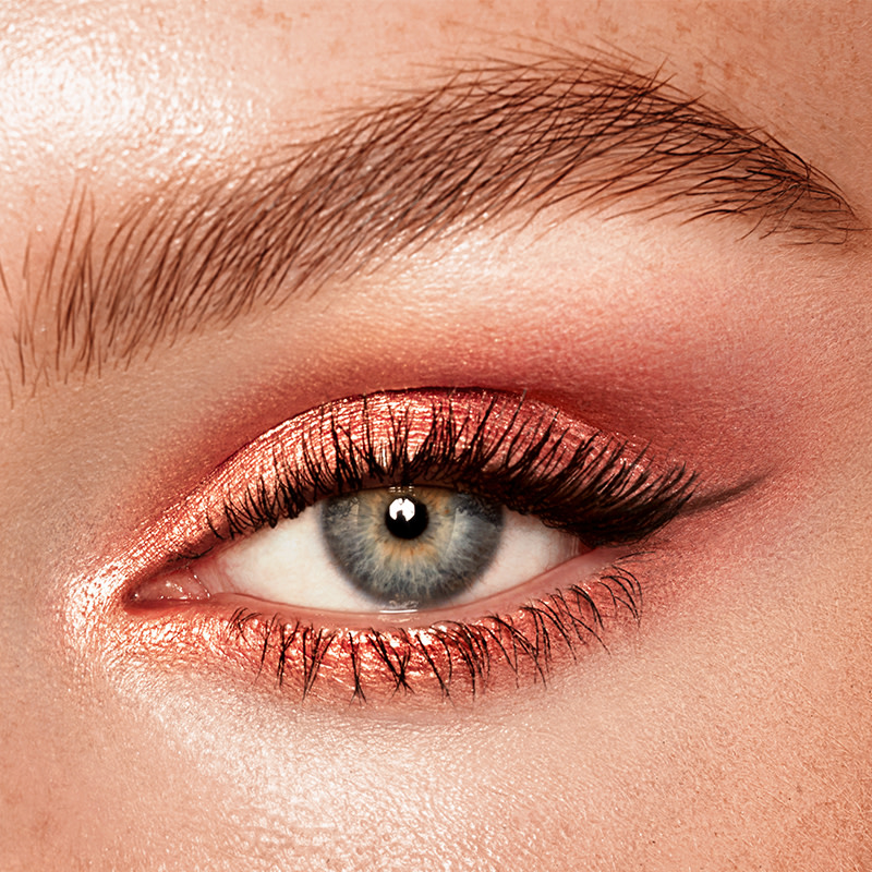 Single-eye close-up of a fair-tone model with blue eyes wearing shimmery rose gold cream eyeshadow.