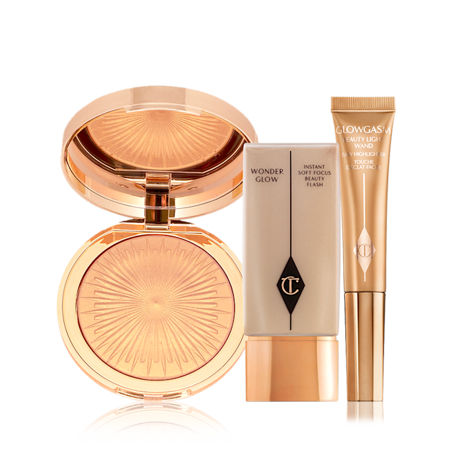 Ibiza Glow Makeup Look displayed An open, mirrored-lid highlighter compact in a soft gold shade, glowy primer in a rectangular, transparent bottle with a gold-coloured lid, and a highlighter wand in a honey-gold shade.