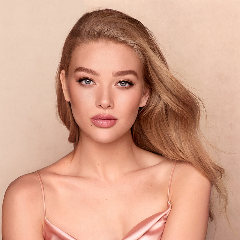 A fair-tone blonde model with flawless, smooth skin wearing matte pink lipstick with soft smokey eyeshadow.